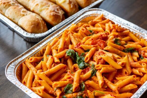 Penne in tomato sauce with spinach, beside a tray of garlic bread